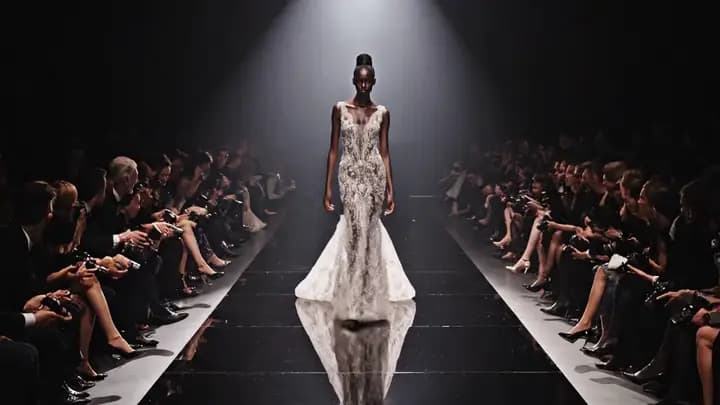 A runway model walking through a dark fashion hall in a portrait-oriented teaser scene.